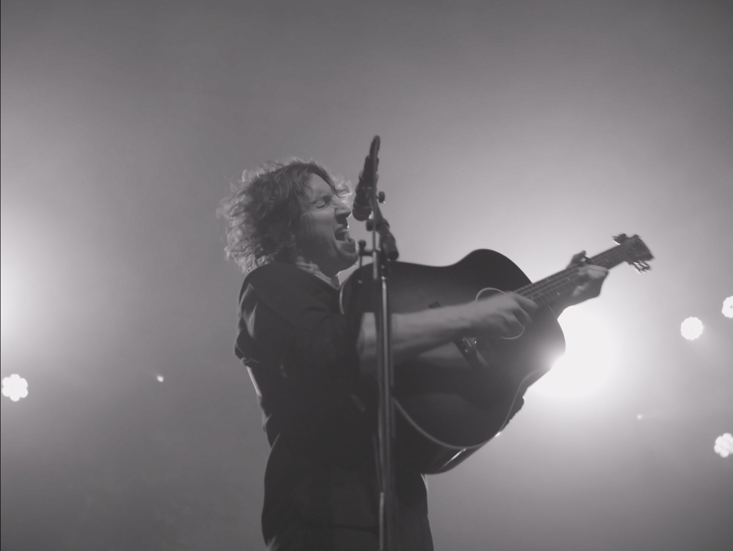 black and white image of man singing and strumming guitar passionately