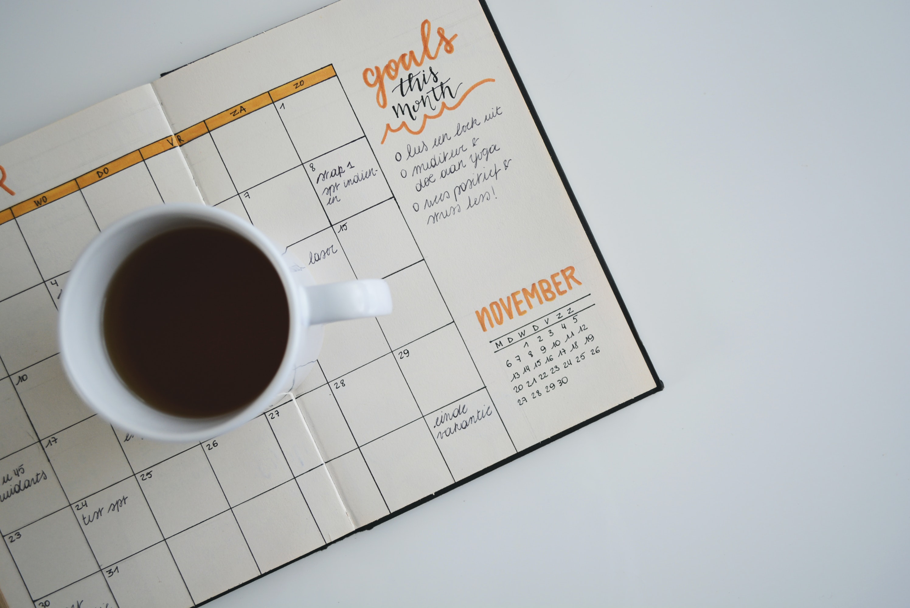 Coffee in a cup placed on top of a notebook. The notebook is lined with a calendar that has been filled out with events.