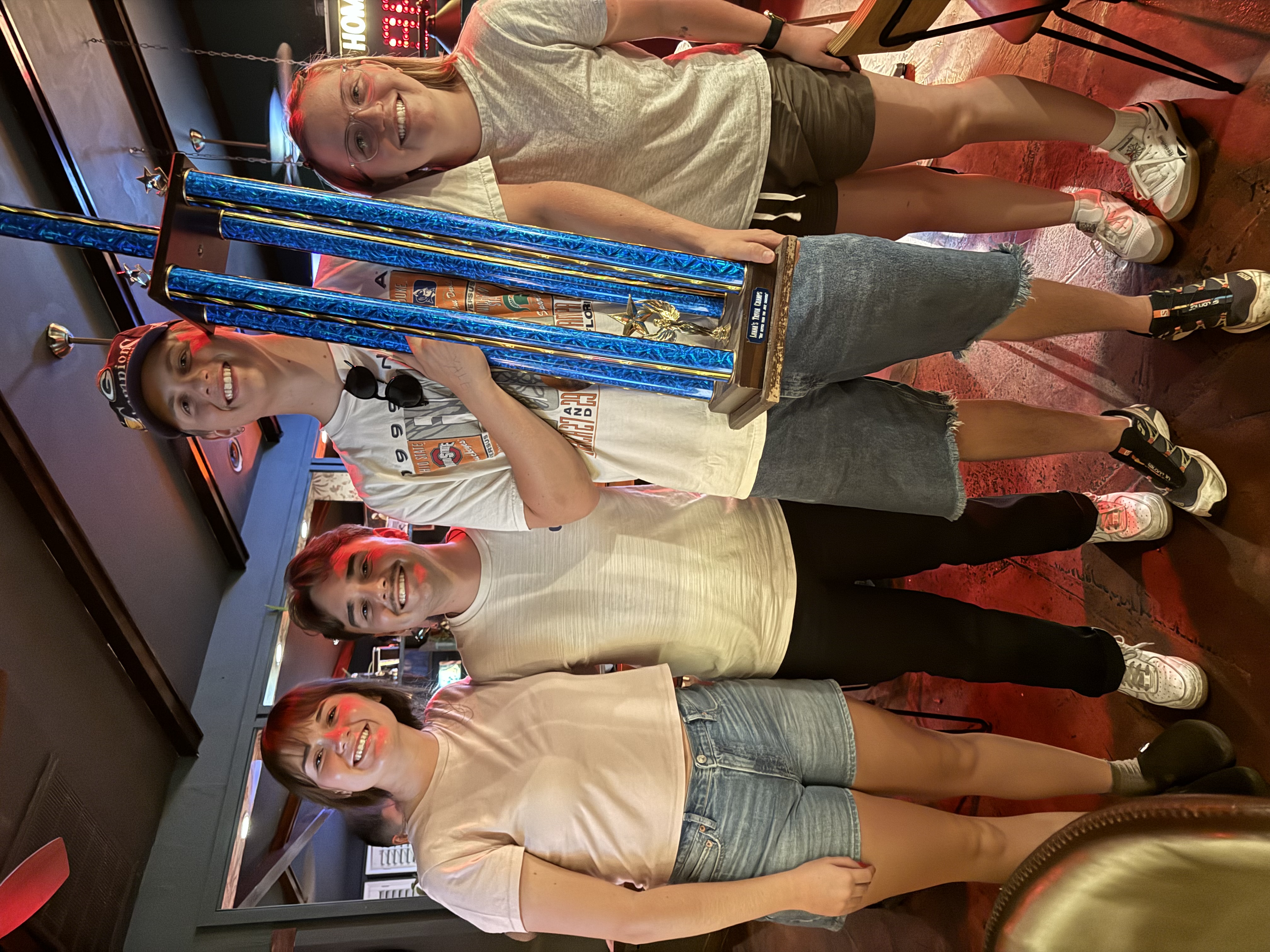 Group of 4 people posing for a picture, one man holding a large trophy