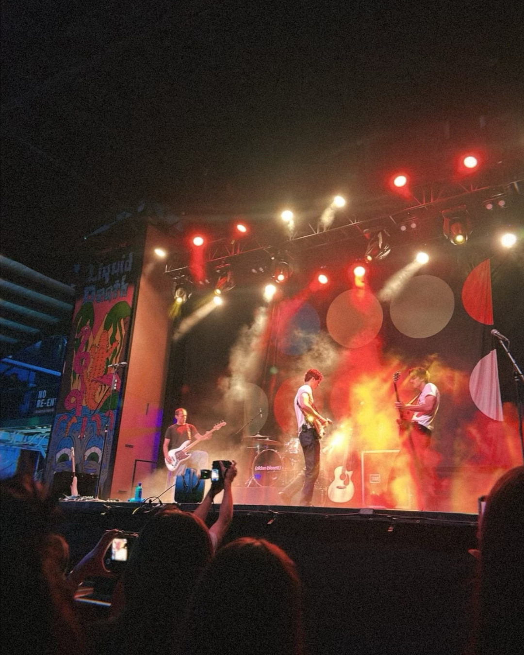three guys on concert stage under orange lights