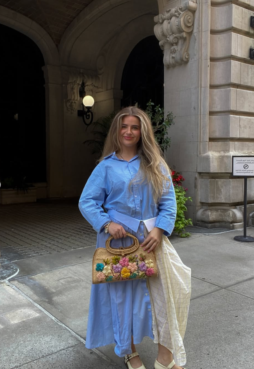 Claudia Campbell smiling for a picture with a colorful outfit and bag.