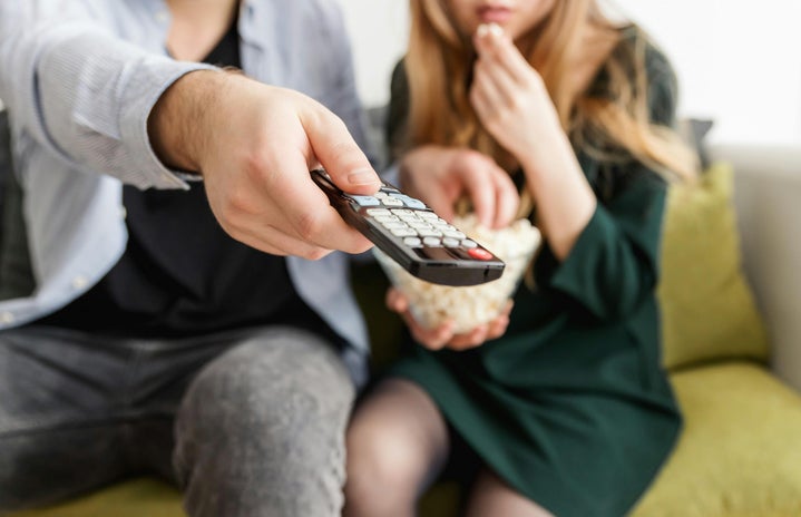 man holding remote with woman in background, watching tv