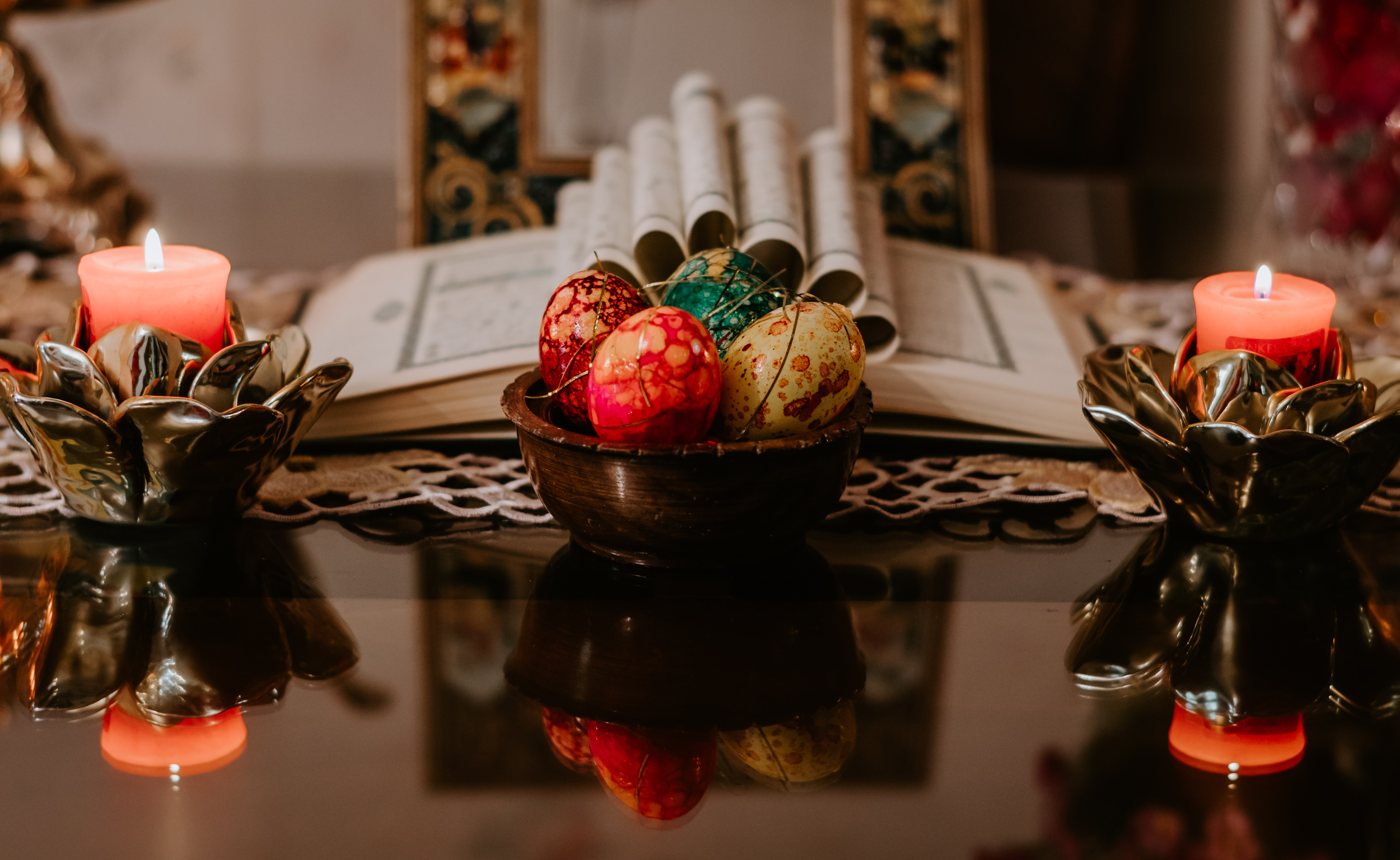 An open book, lit candles, and colorful eggs on a dark brown table
