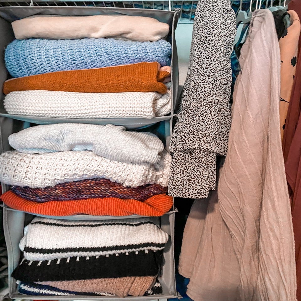 sweaters in cubbies and next to that is hanging skits and shirts in a closet