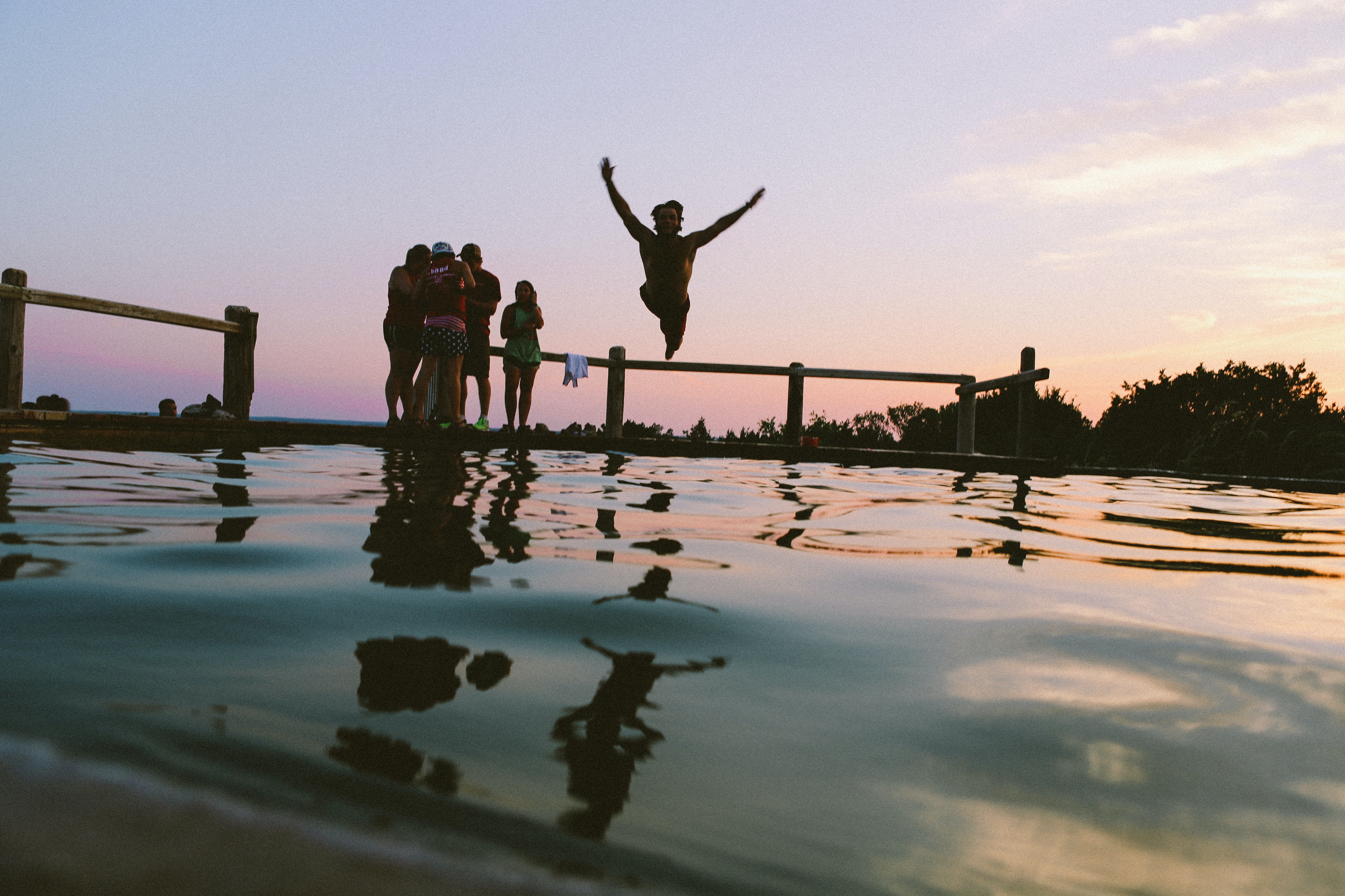 person jumping into body of water as their friends watch