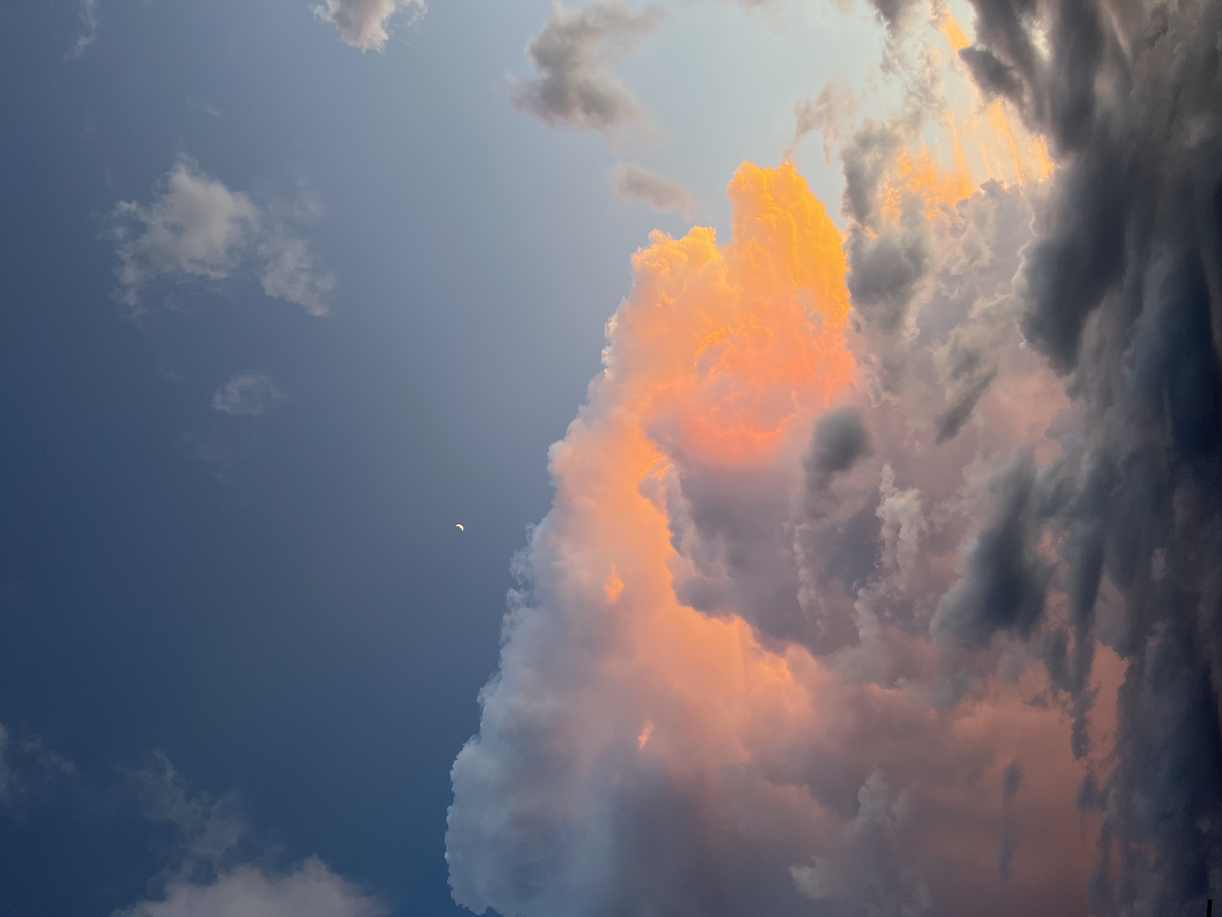 The moon next to clouds in a sunset.