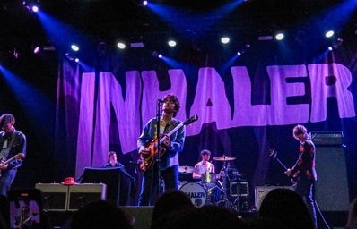 Stage occupied by four musicians, with a black backdrop that says \"Inhaler\"