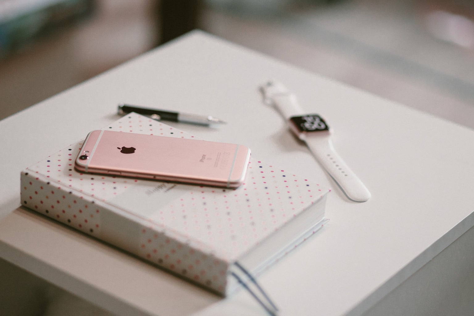 Rose gold smartphone on top of white white covered book with smartwatch