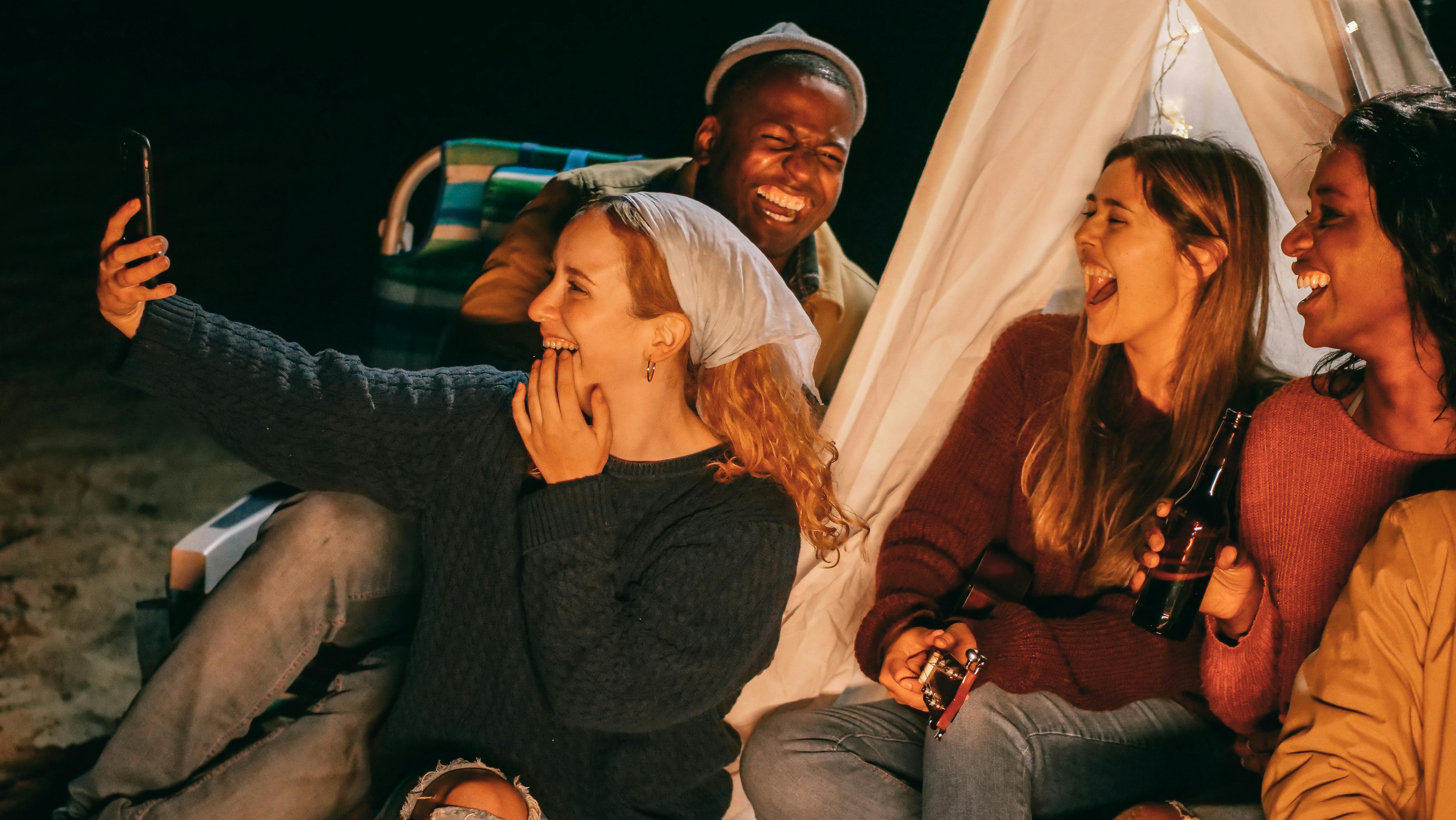 friends sitting at camp fire tkaing pics