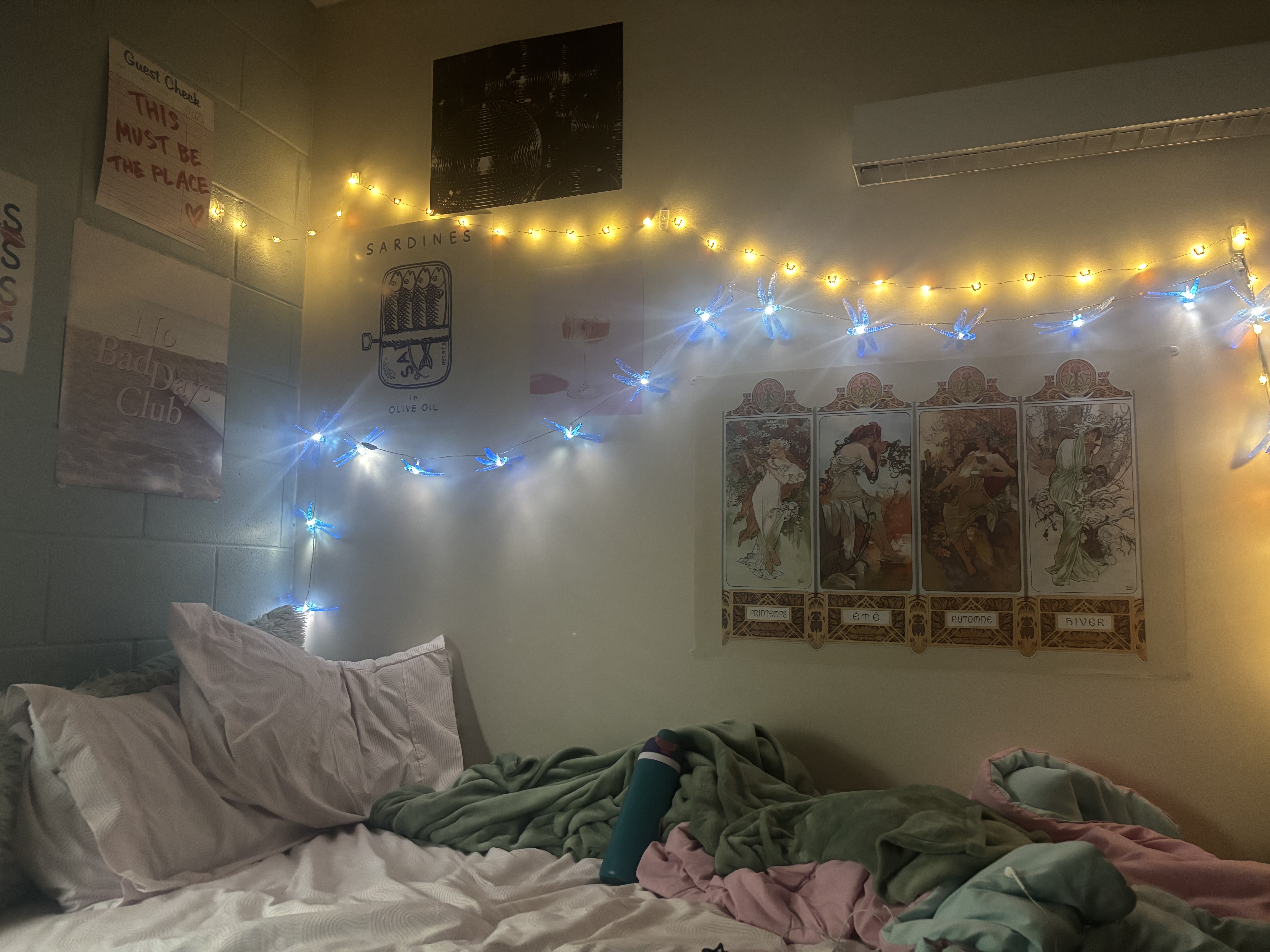 A dorm wall with a variety of posters and string lights