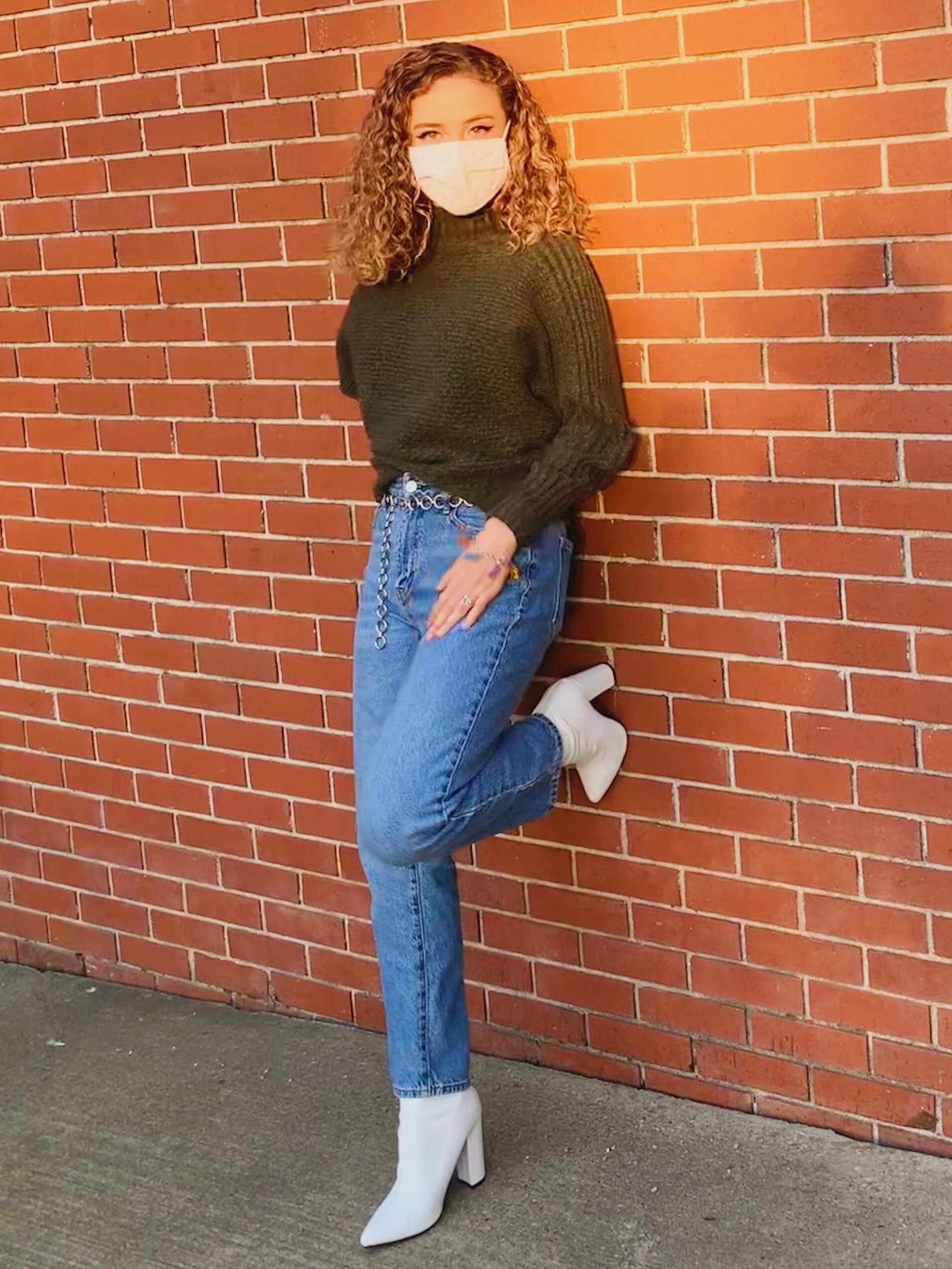 Girl in green sweater leaning on wall.
