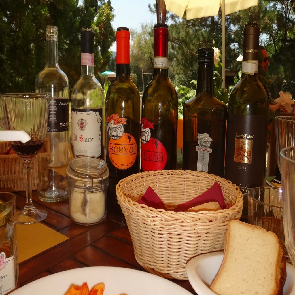 The image shows a table set with several wine bottles, glasses, a basket of bread, and other dining items.