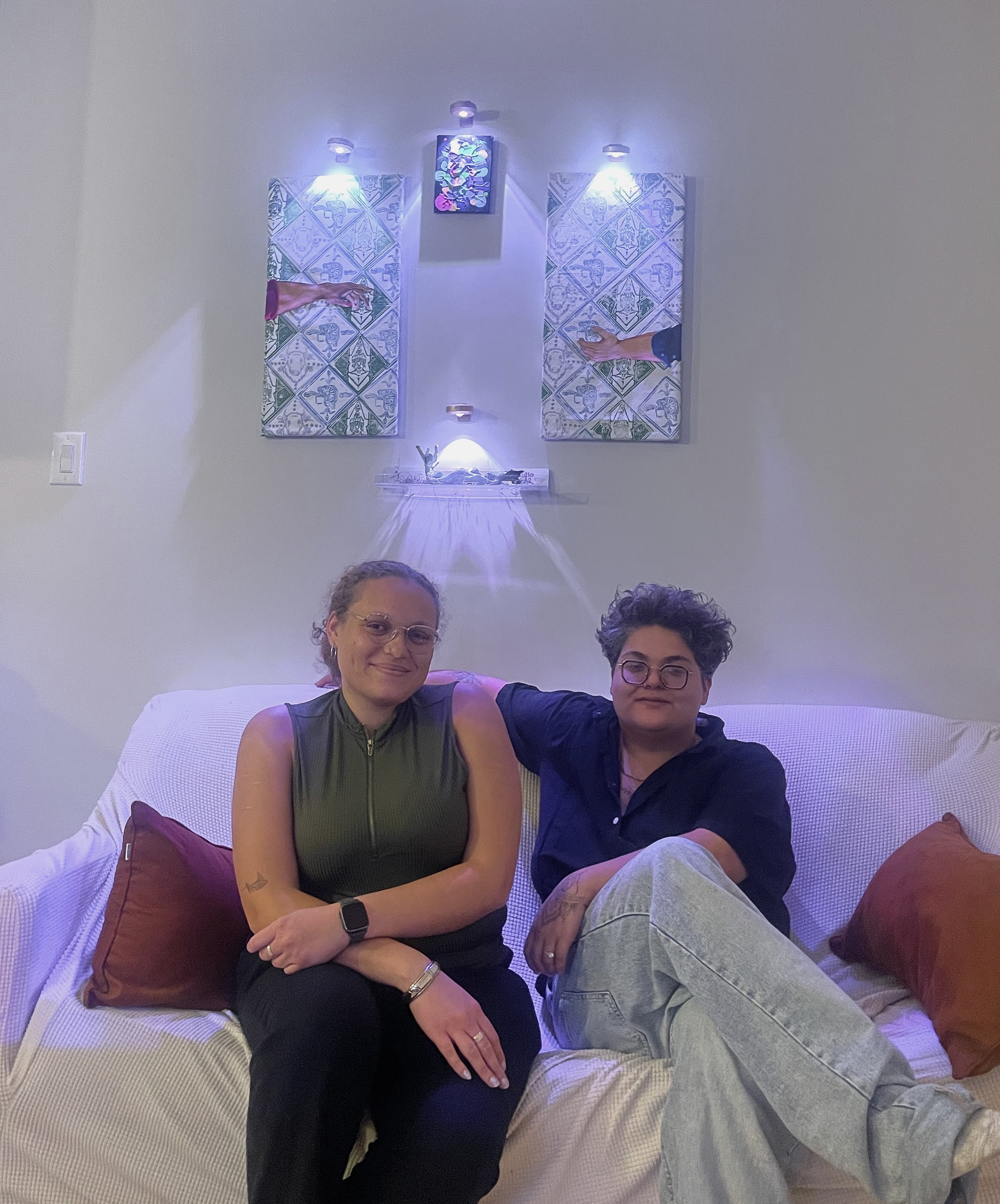 two artists sitting on a couch, with art hanging on the wall behind them
