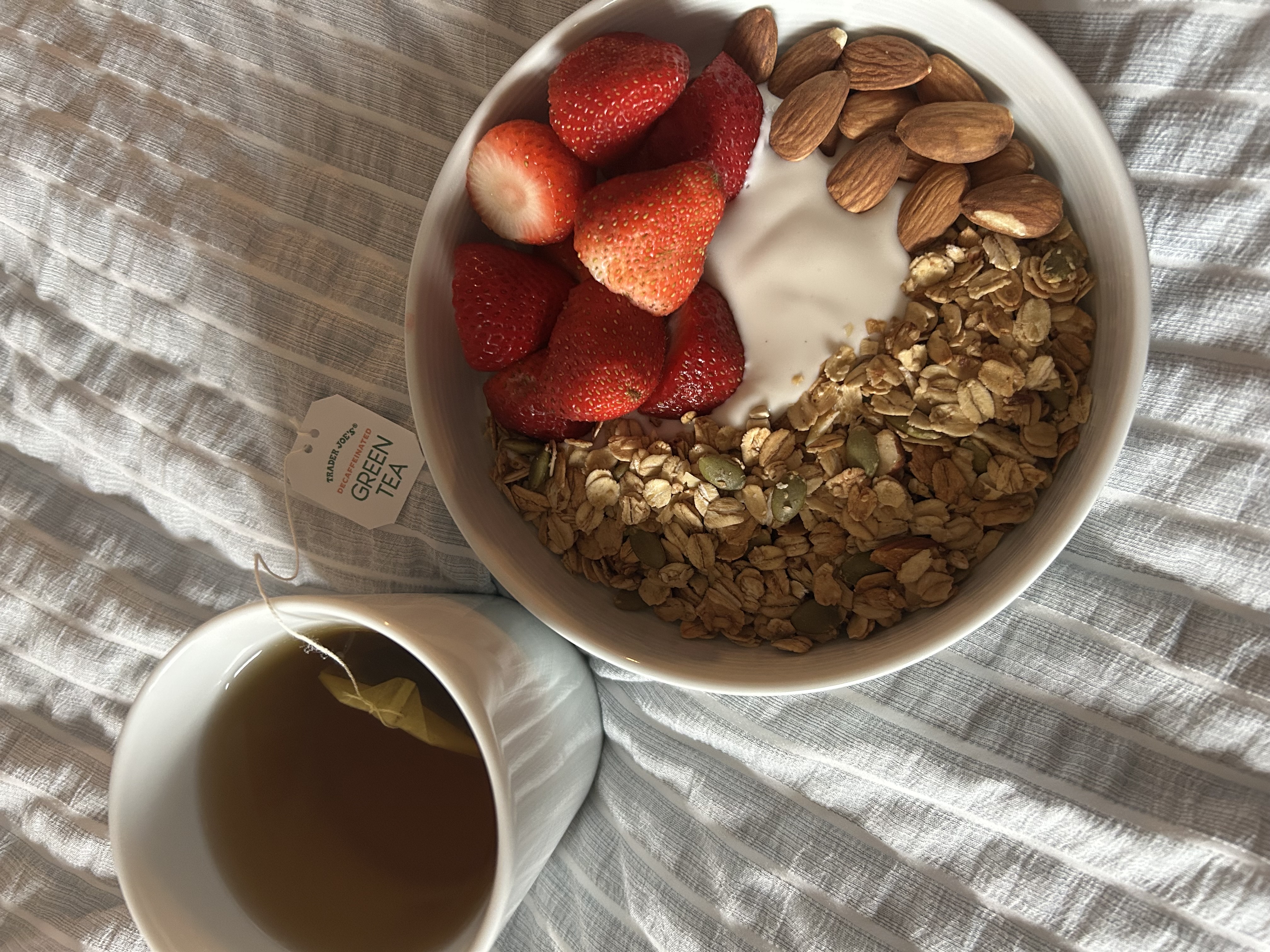 Yogurt bowl with strawberries, granola, and green tea on the side