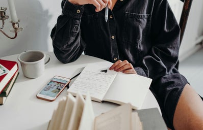 Person sitting on wooden chair at table with open book and pencil.