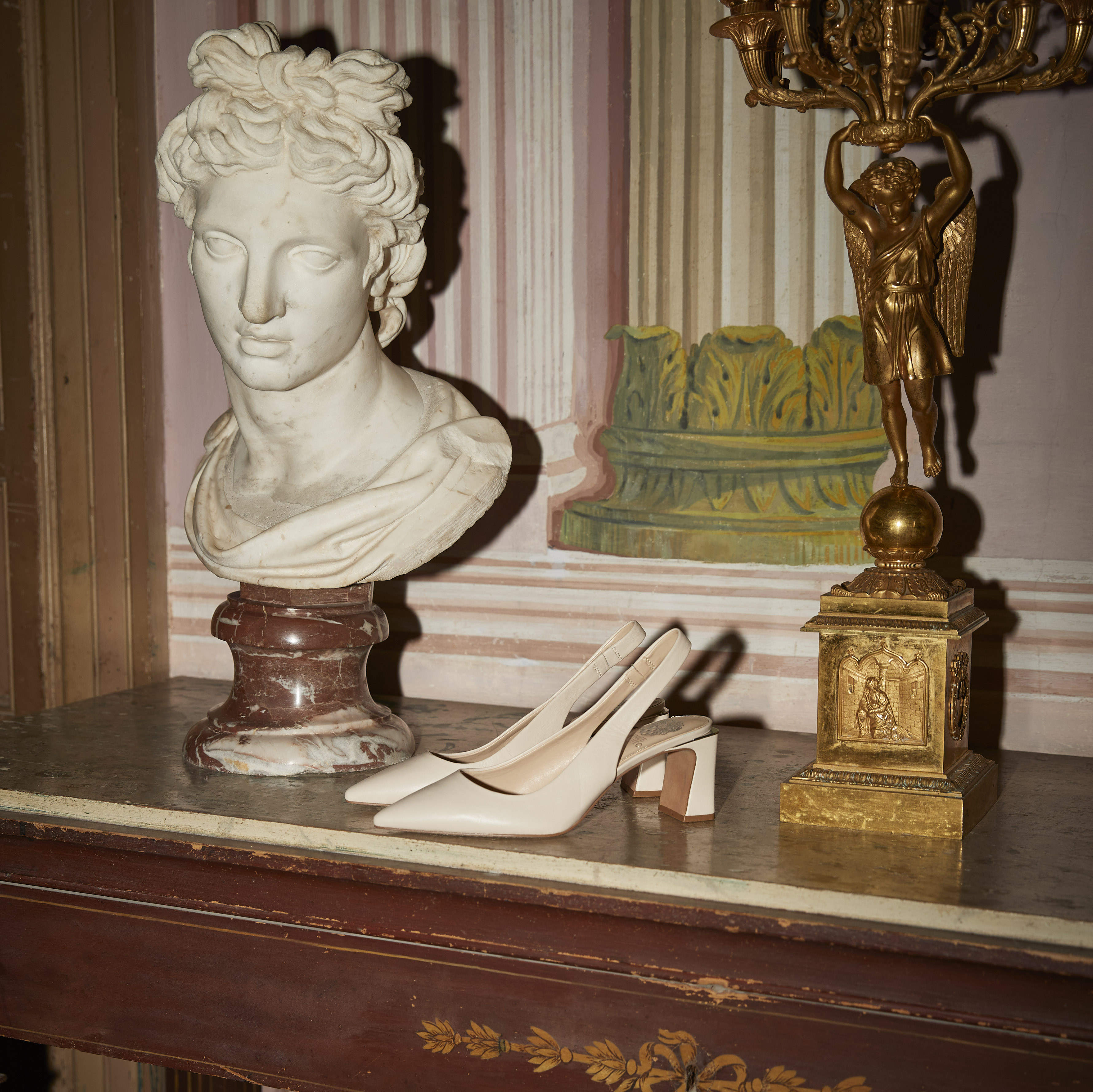 White slingback heels on a dresser next to a marble bust and gold figurine