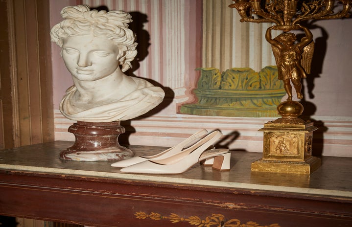 White slingback heels on a dresser next to a marble bust and gold figurine