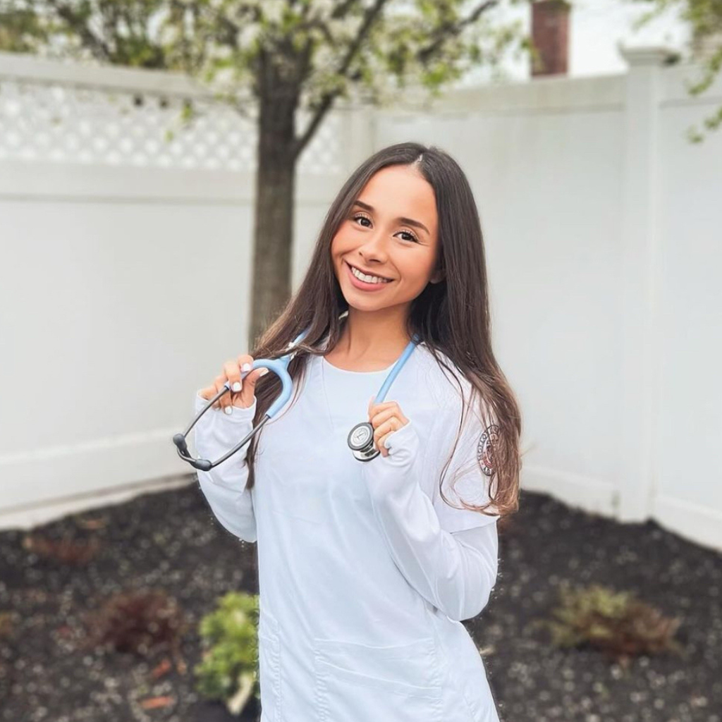 woman with long brown hear wearing white nurse scrubs and holding a stethoscope