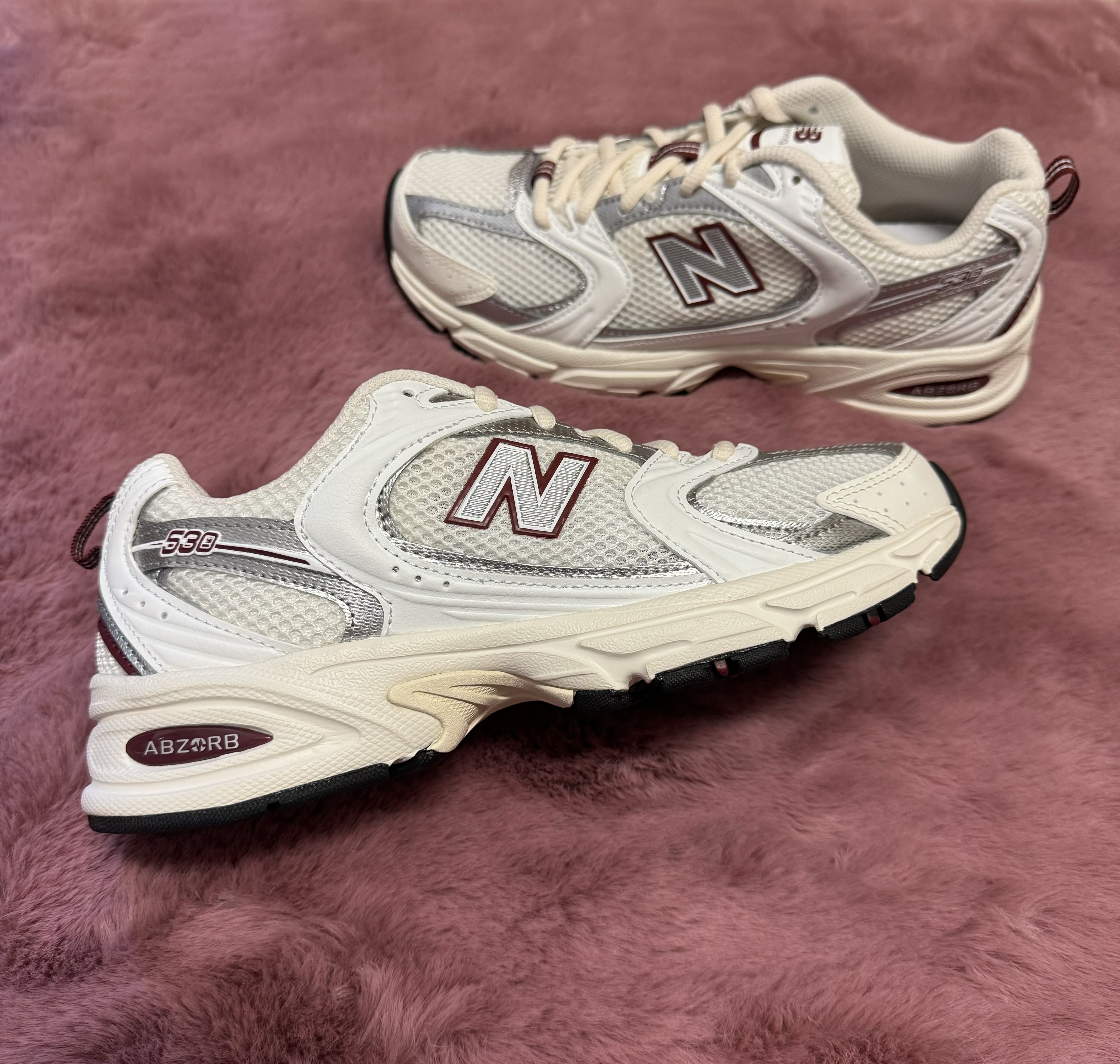 A pair of New Balance 530 shoes over a pink rug.