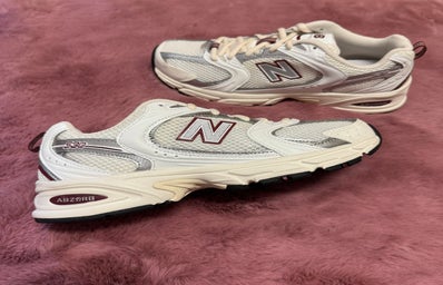 A pair of New Balance 530 shoes over a pink rug.