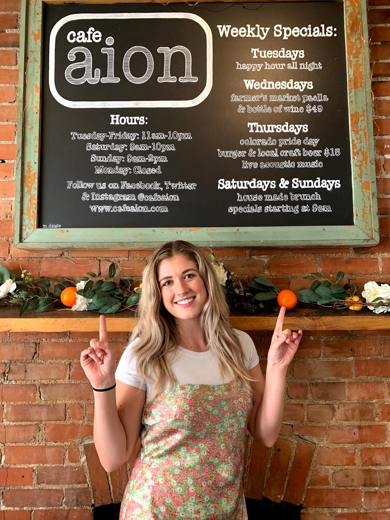 Kaitlyn standing in front of fireplace pointing up at the sign for Cafe Aion