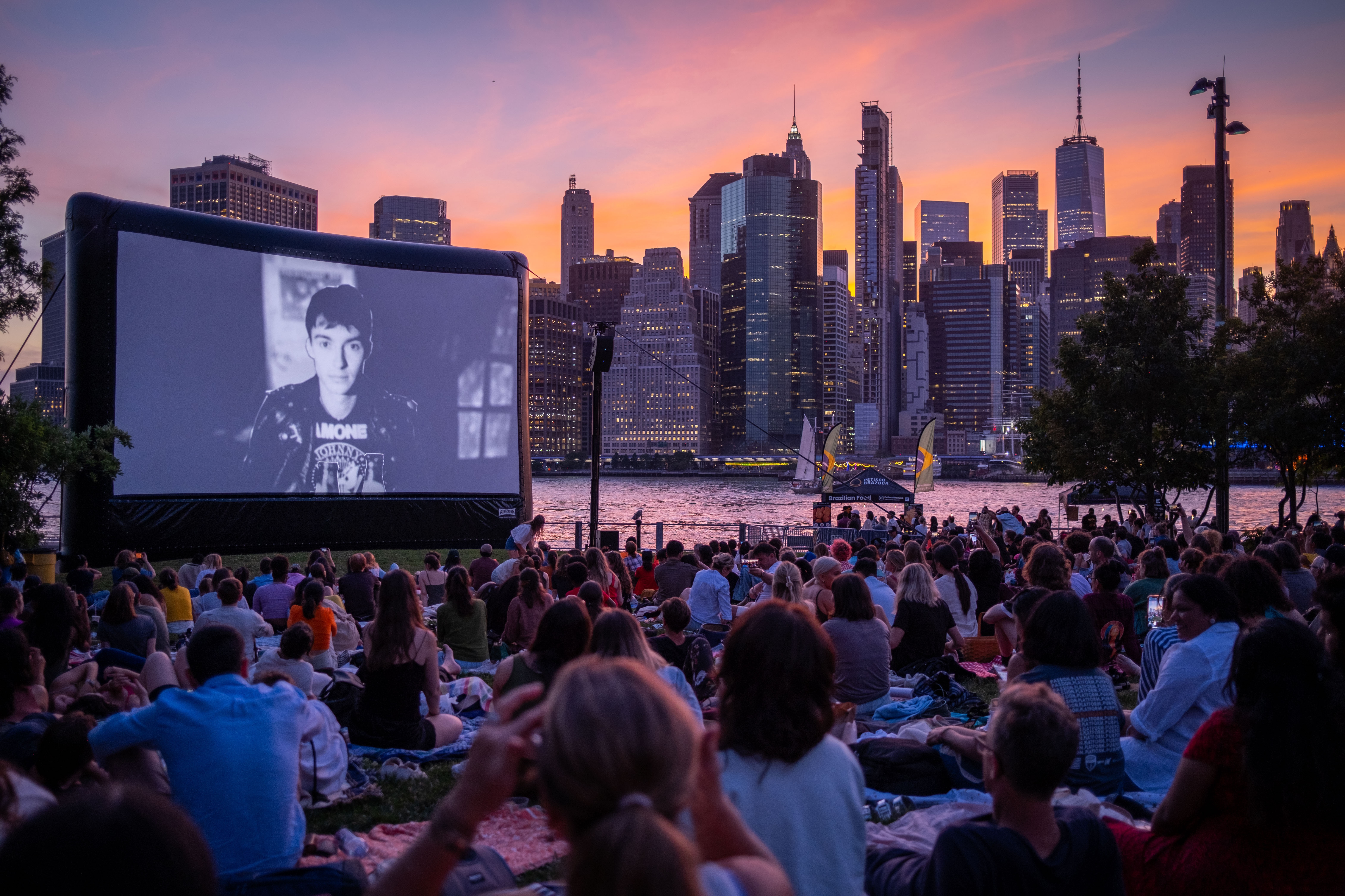 Crowd watching drive in movie, sunset in the background, movie is in black and white