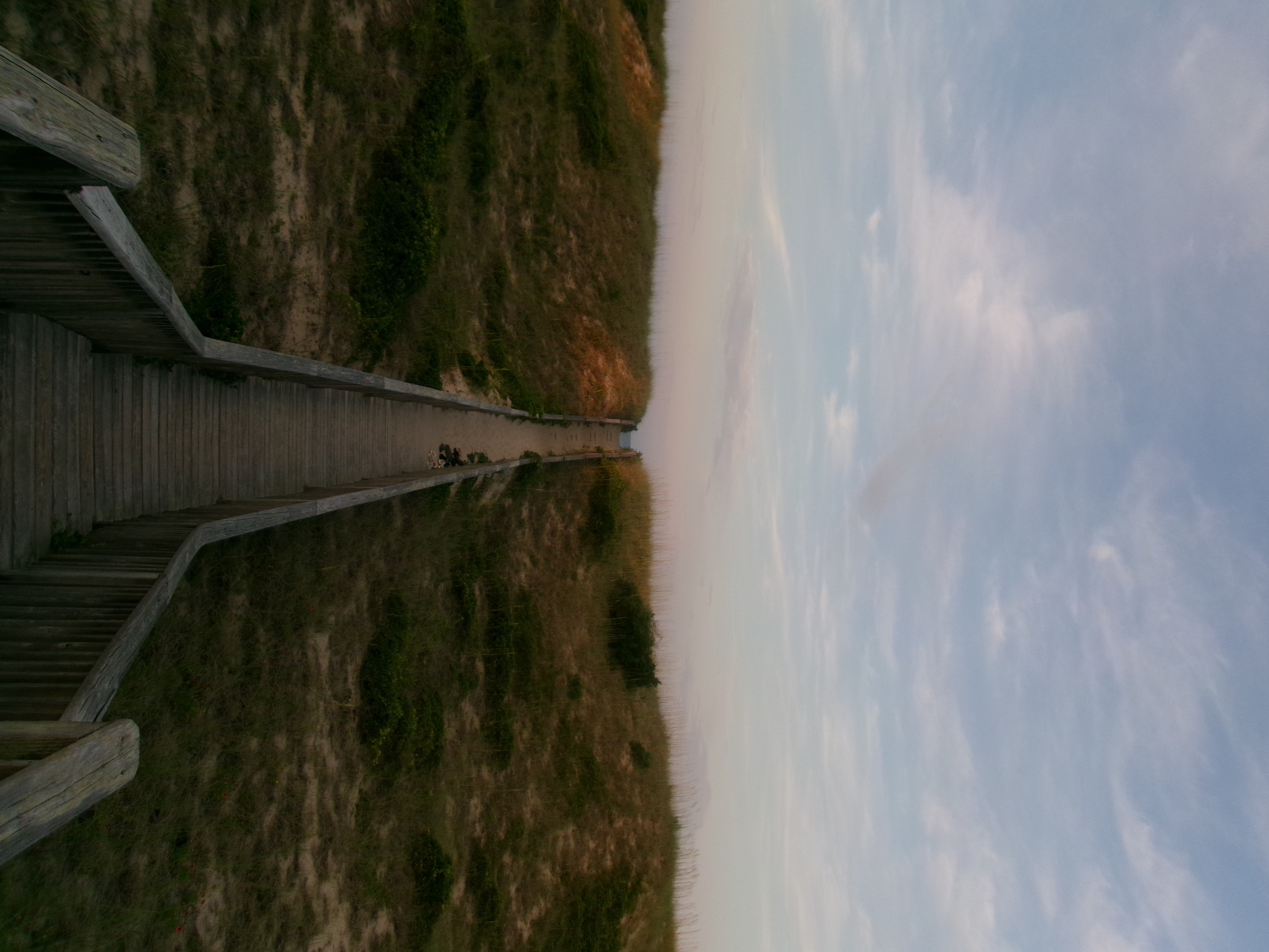 A wooden pathway leads to the beach as the sun sets.