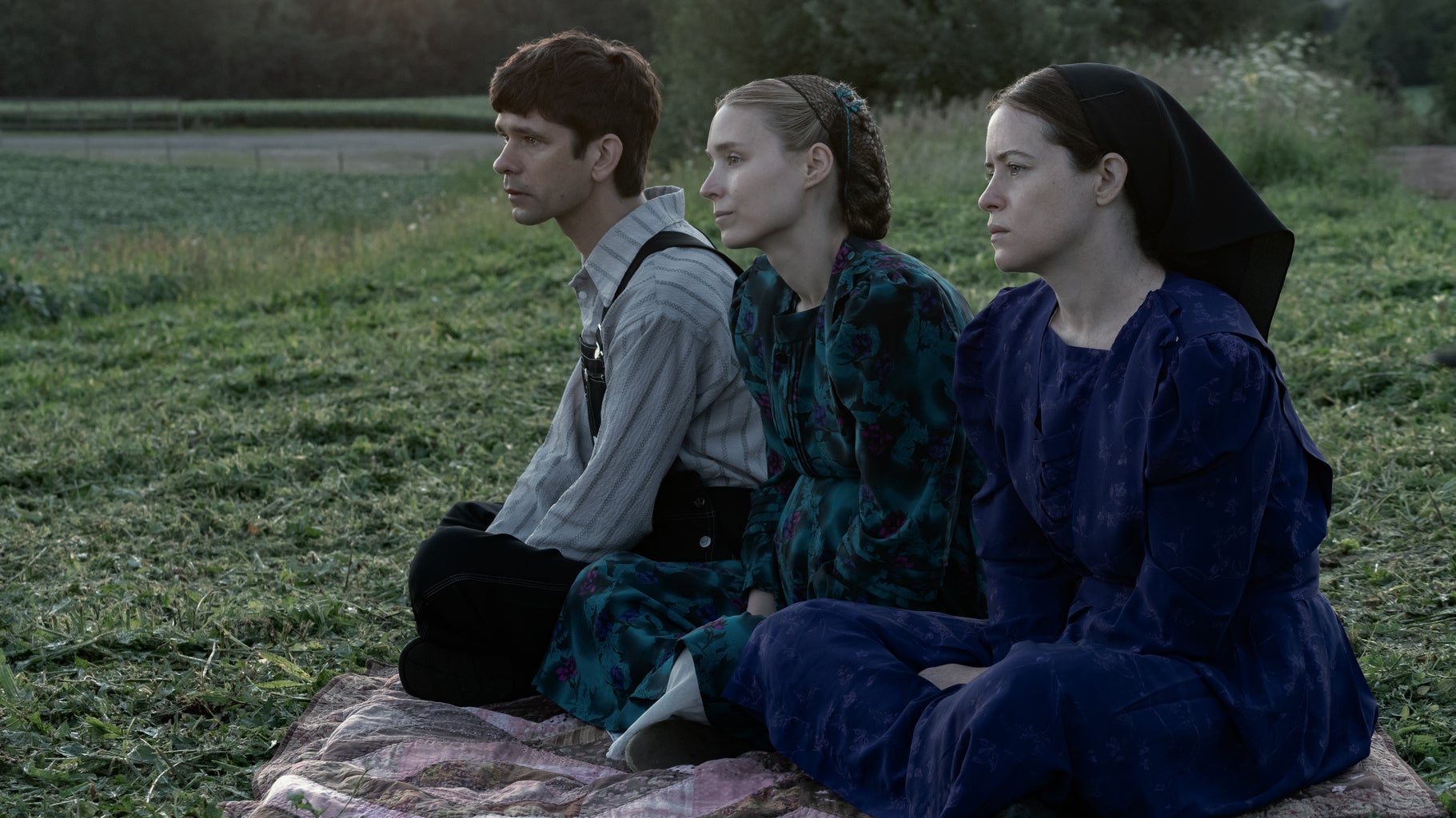 two women and one man in modest clothing sitting on a picnic blanket