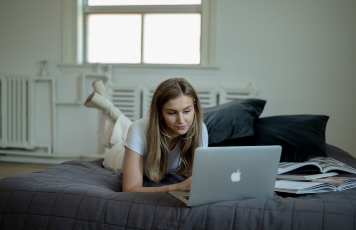 Woman in white laying in bed looking at laptop.