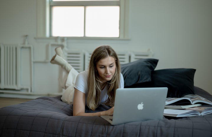 Woman in white laying in bed looking at laptop.