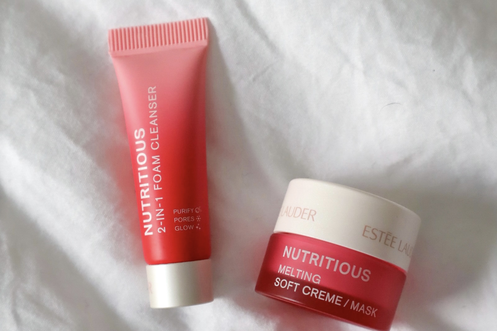 Estée Lauder cleanser and melting mask laying on a white bed spread