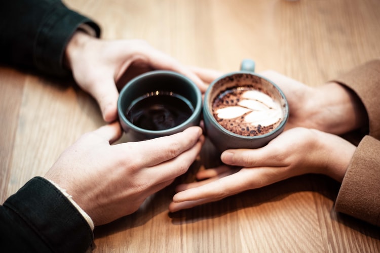 two people holding coffee mugs on table