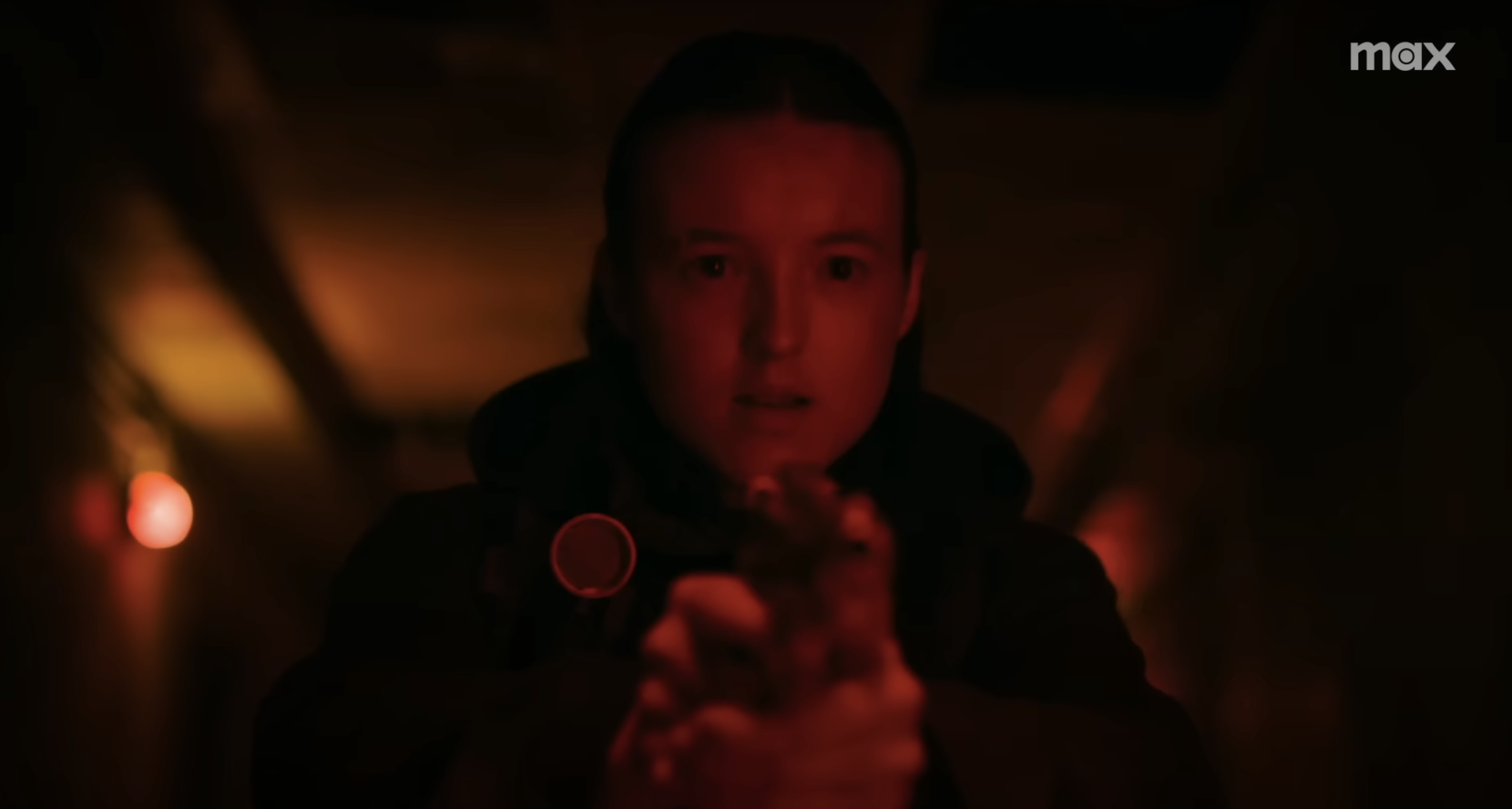 A woman (Bella Ramsey) pointing a weapon towards someone off camera. Still image from \