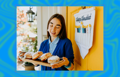 woman holding plate of sufganiyot (jelly donuts) next to happy hanukkah sign