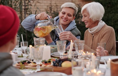 woman pouring a glass from a pitcher for older woman at dinner table