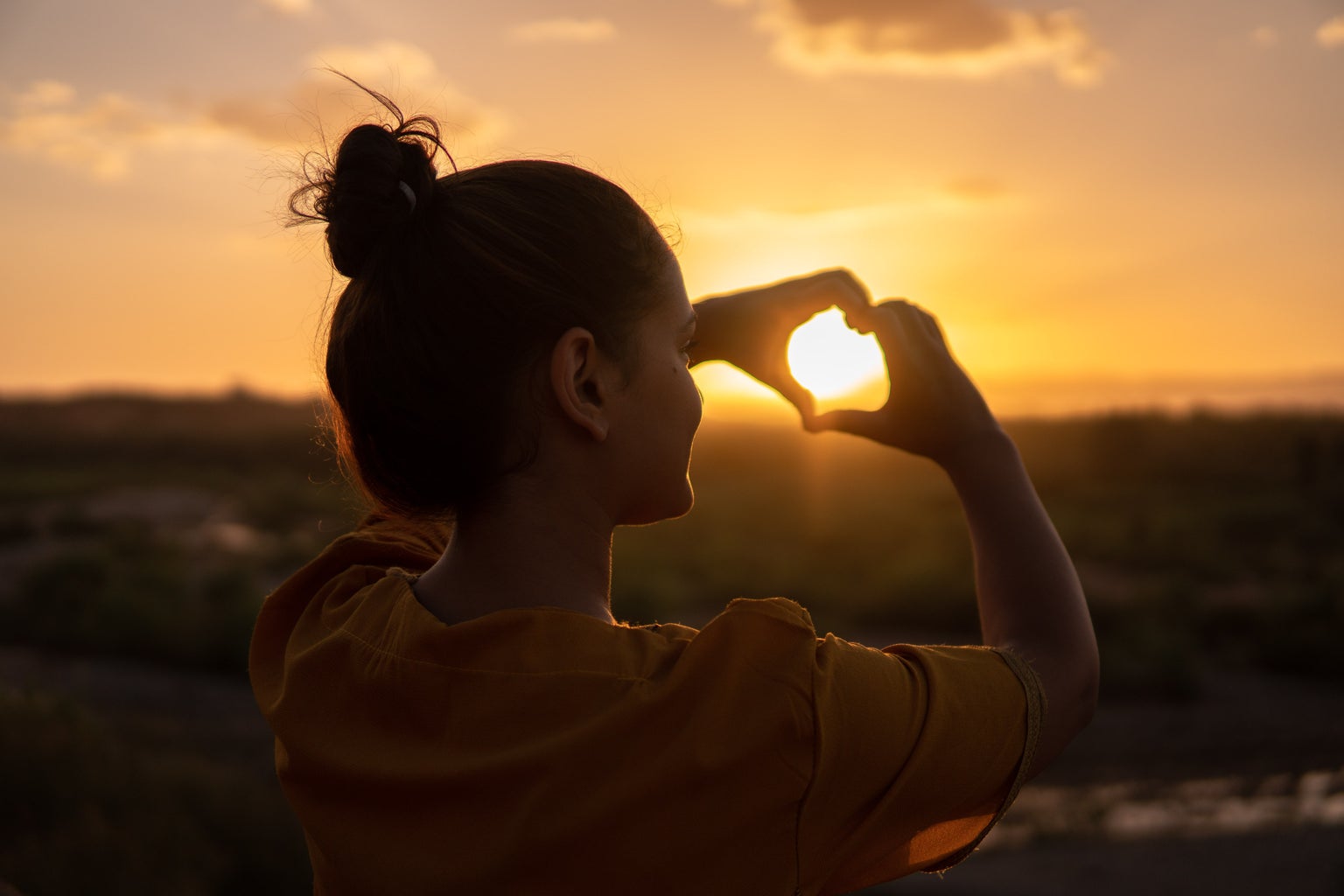 girl making a heart with her hands over a sunset