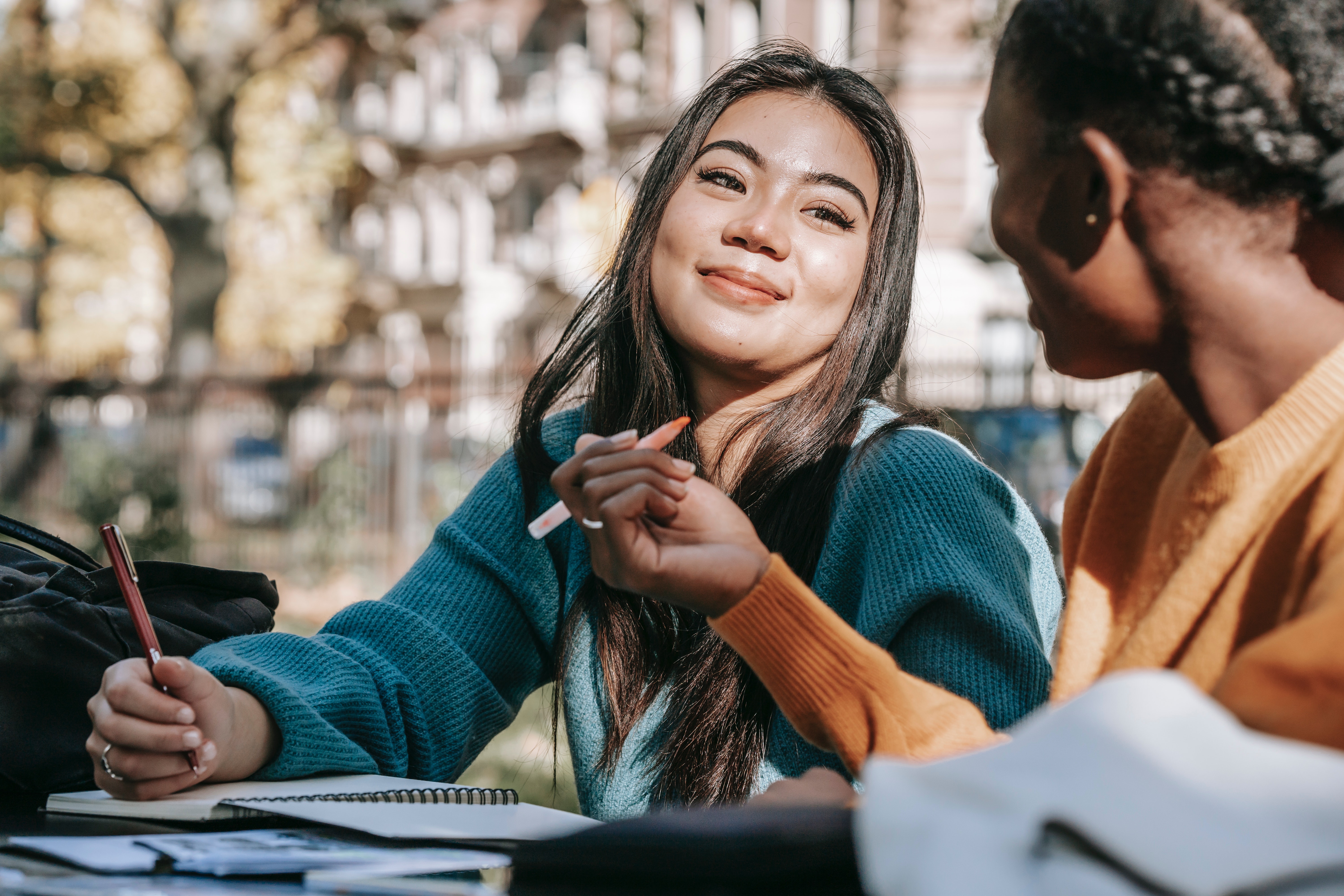 smiling student taking notes outside with friends