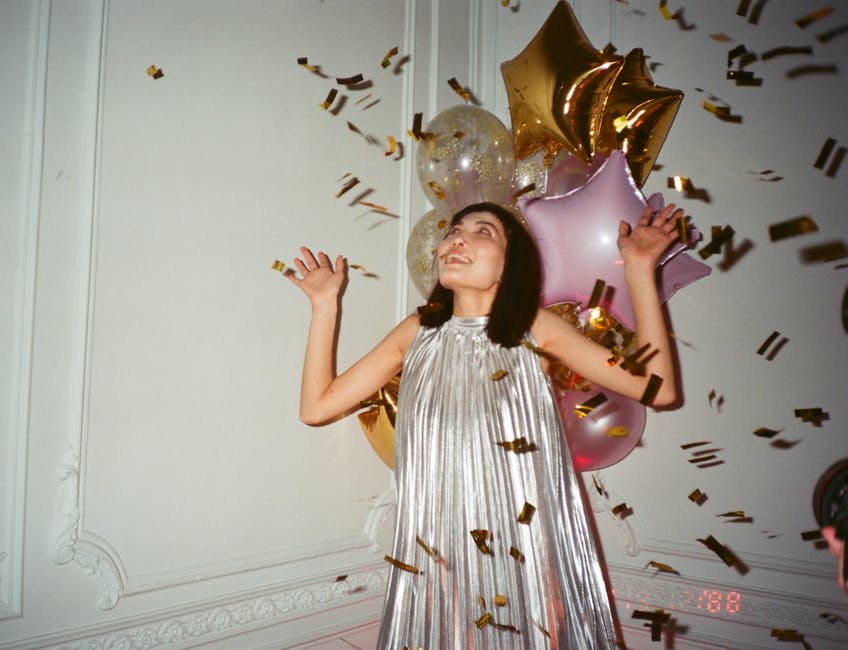 A girl in a silver dress with gold confetti and pink and gold balloons surrounding her