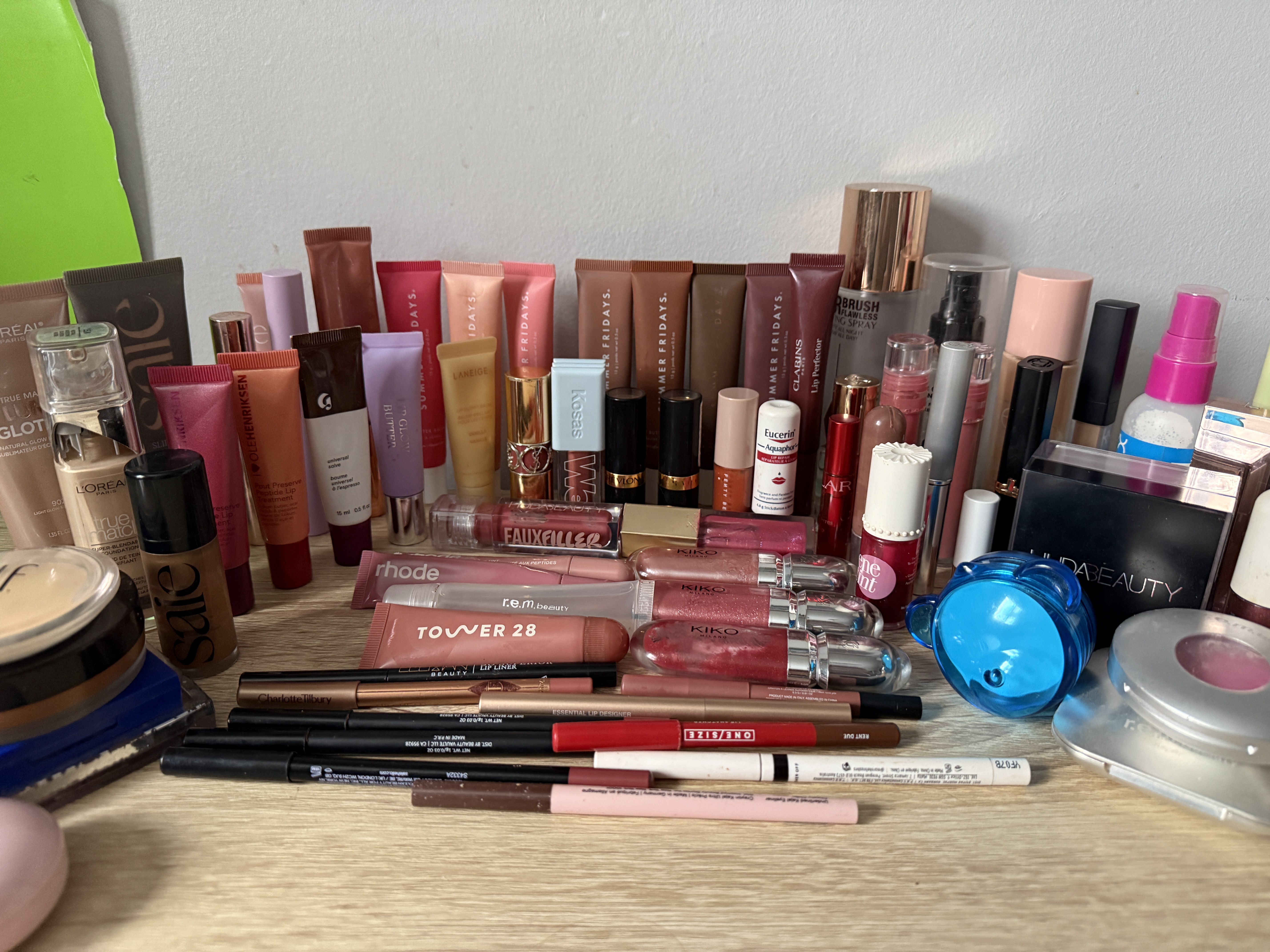 An assortment of cosmetic products is laid out on a desk that someone may want to Project Pan by the end of 2026. The total cost of all the products in this image is $1,829.99