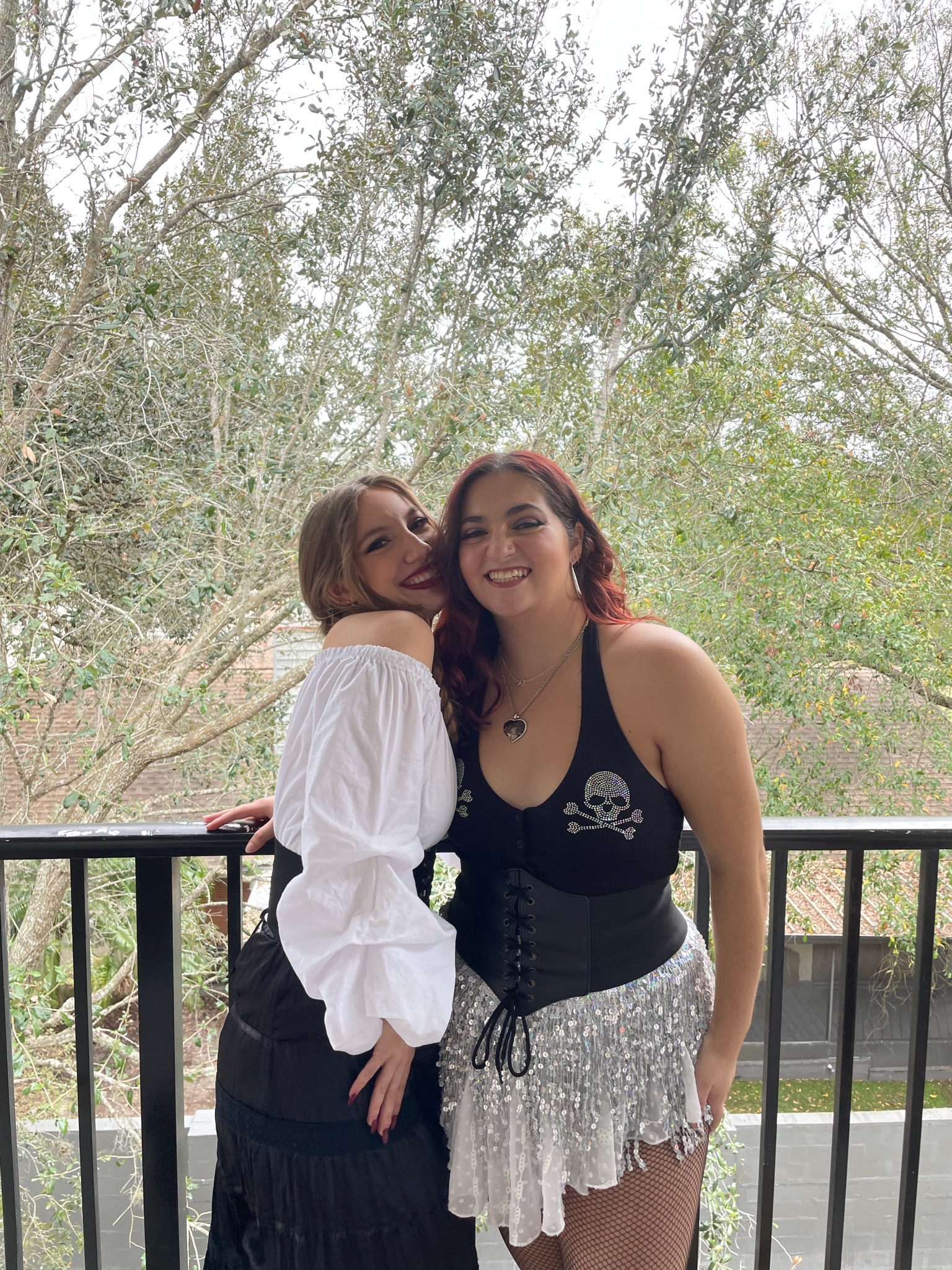 Two women (me and my roommate) stand on our balcony laughing for a picture in pirate outfits.