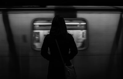 Woman wearing a coat standing on a subway platform watching a train pass by.