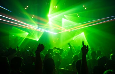 People dancing in a club while a dj is playing electronic music with lasers