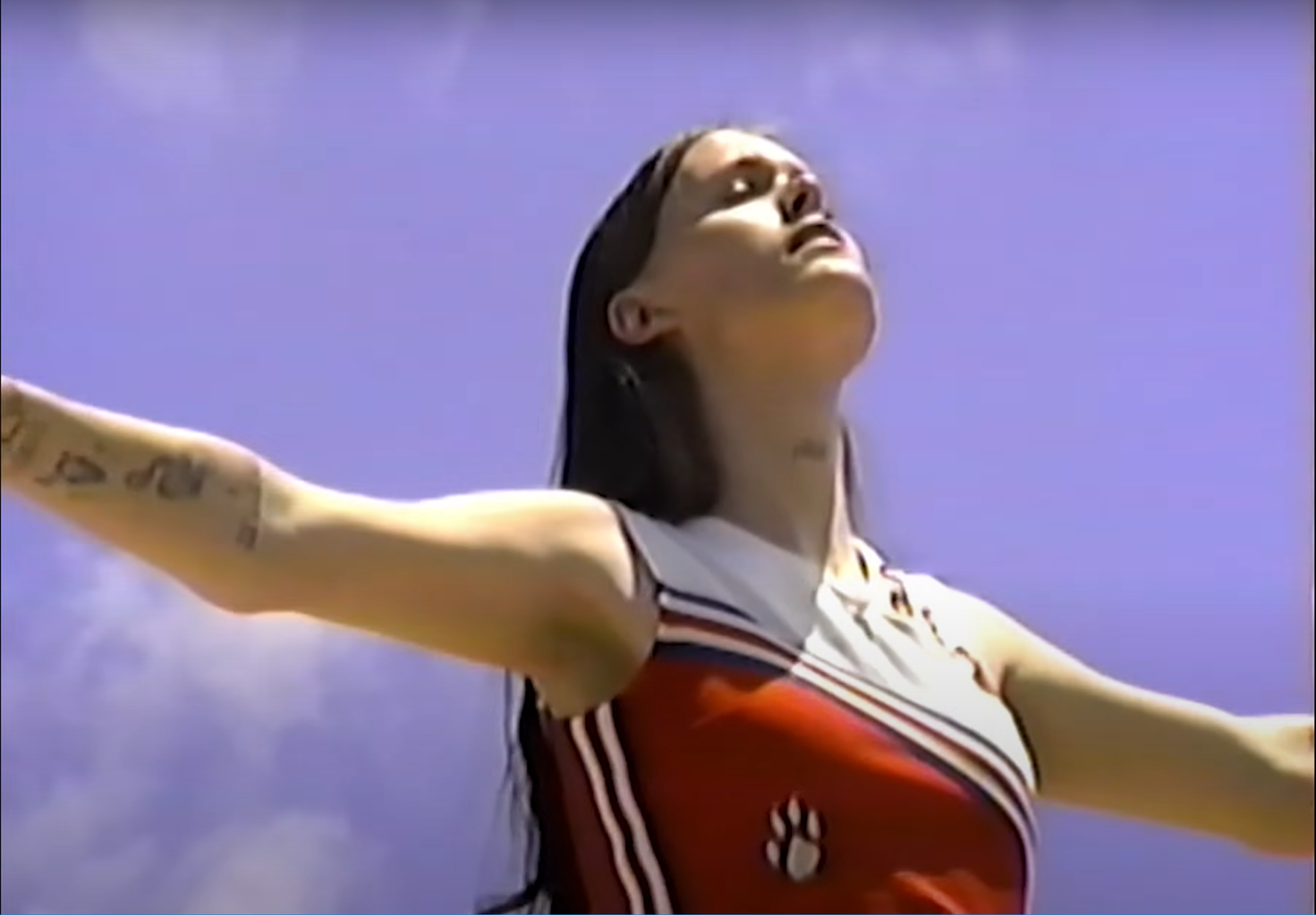 EThel Cain (young white woman) smiles while she looks up at the blue, clear sky. Her arms are extended parallel to the ground.