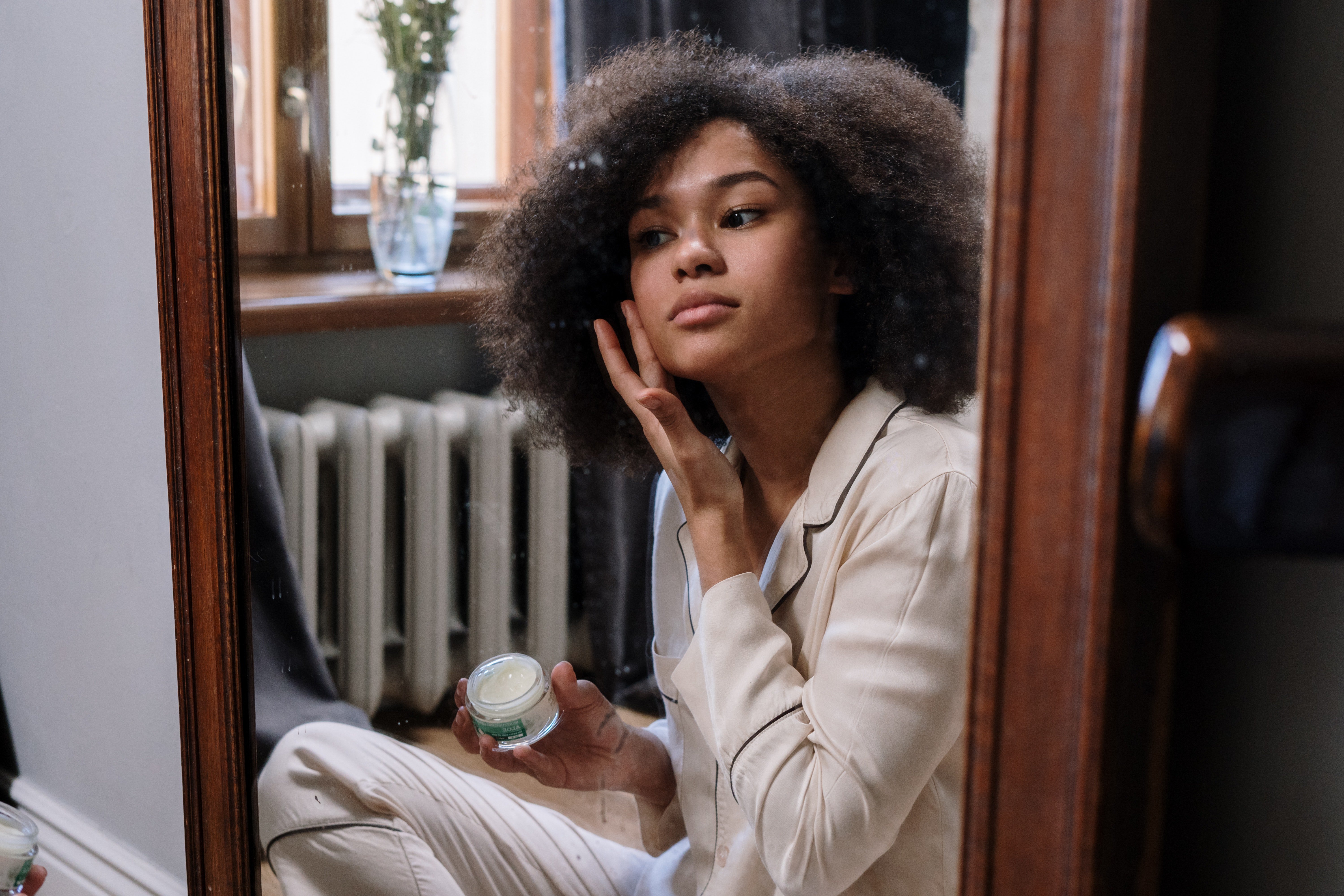 woman applying face cream in front of a mirror