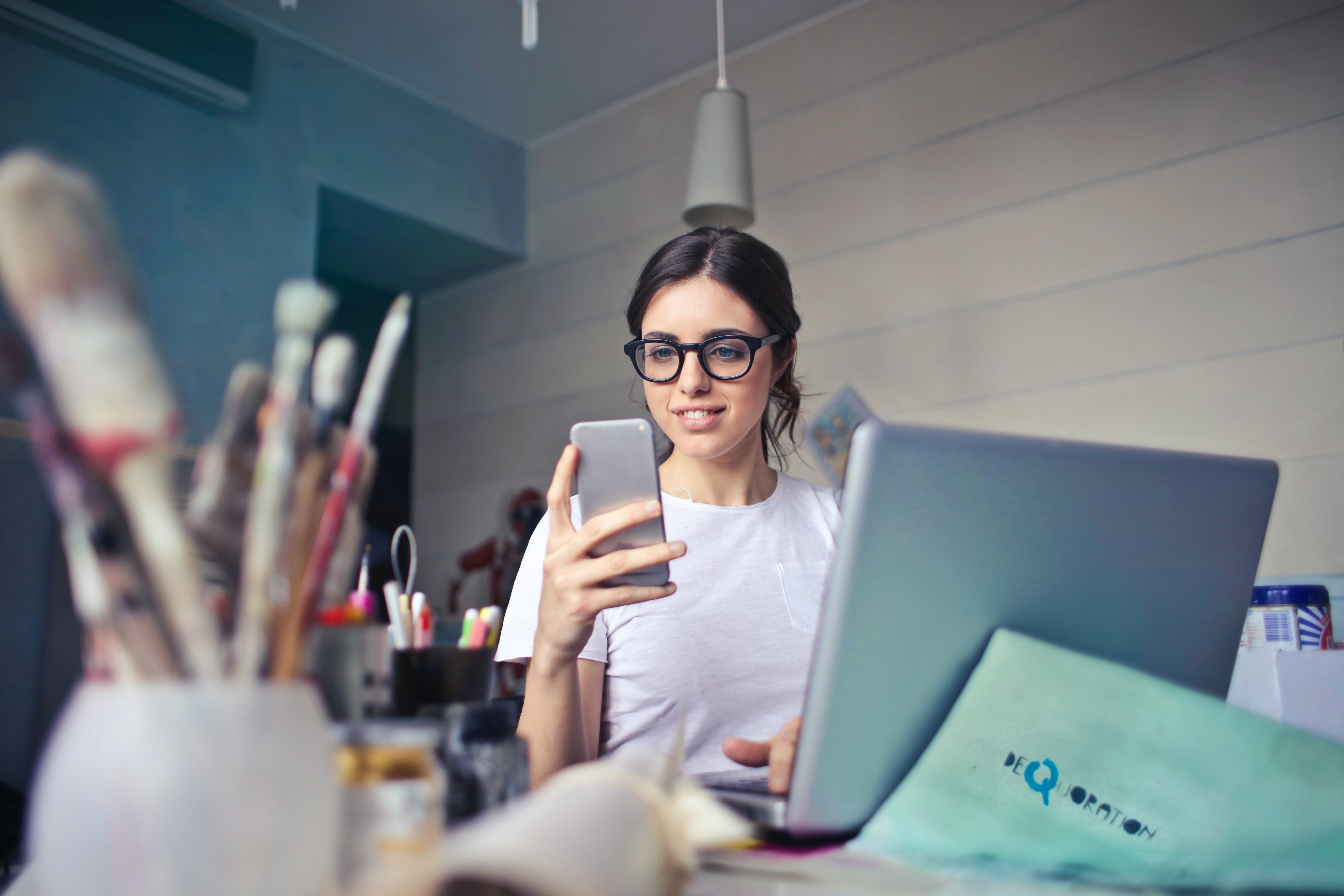 woman with glasses looking at phone on computer