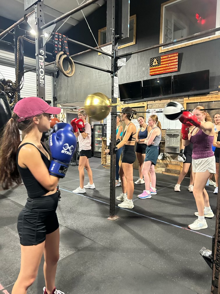Girl wearing boxing gloves in indoor gym surrounded by other girls