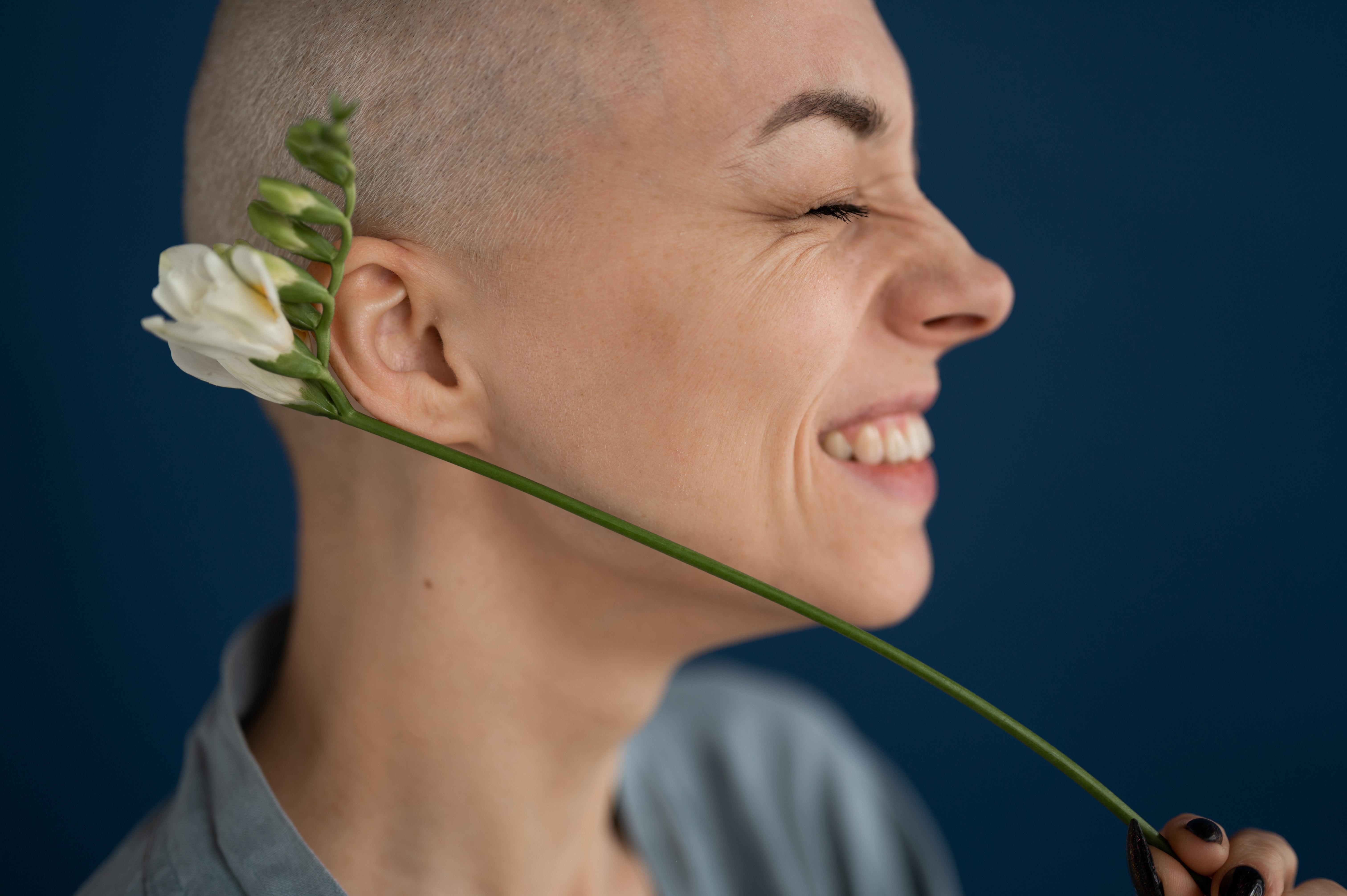 Smiling woman holds flower to her head.