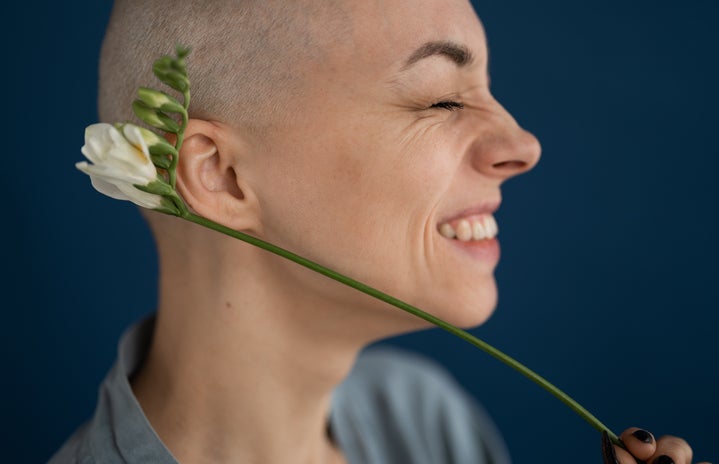 Smiling woman holds flower to her head.