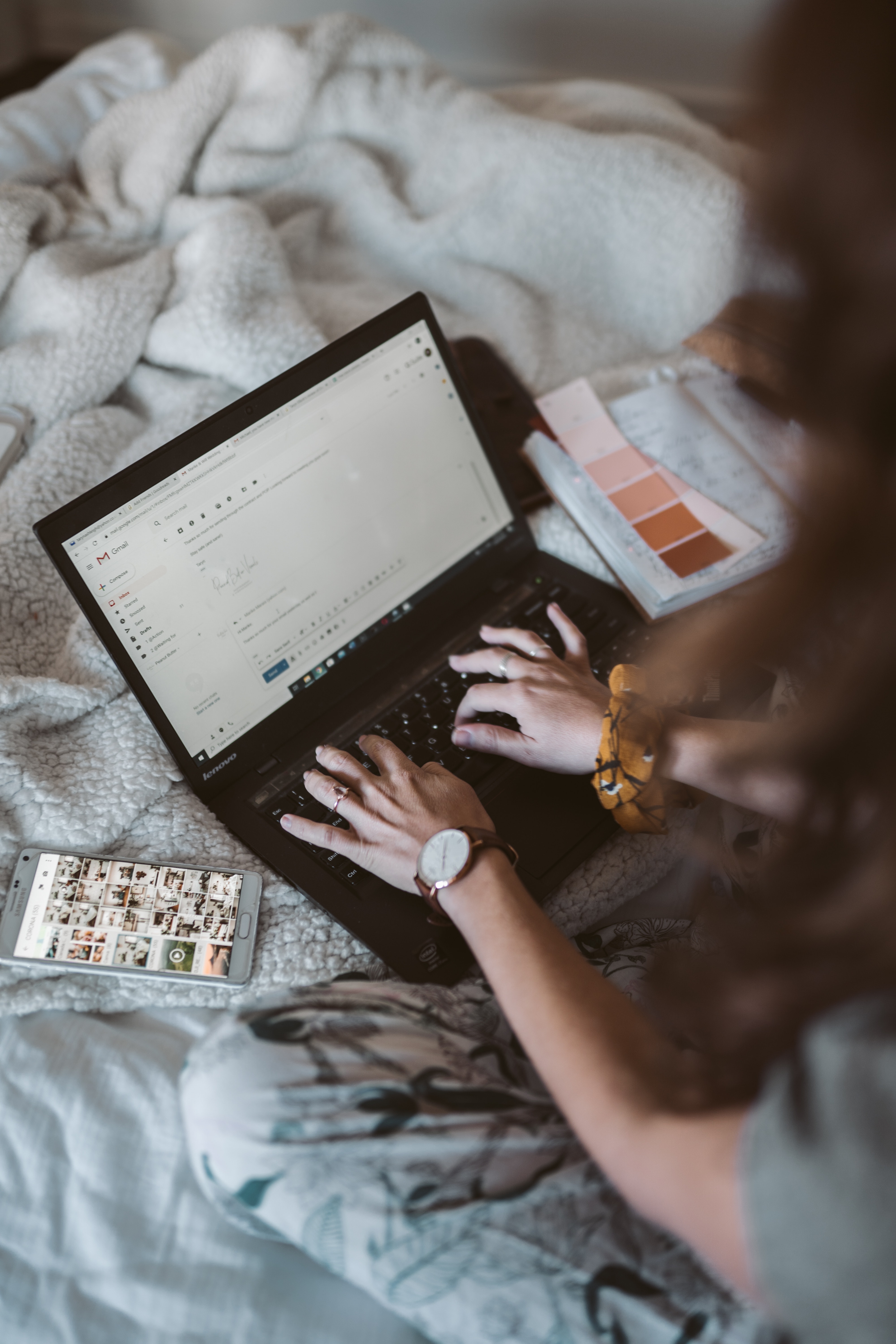 A woman writes an email on her bed.