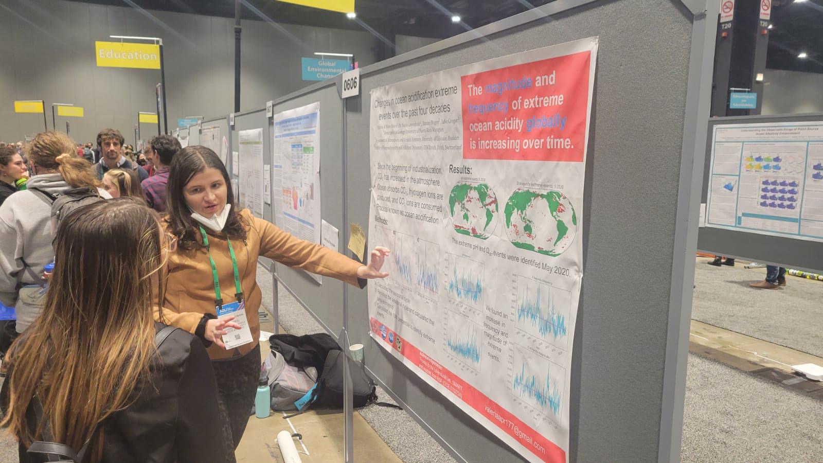 This is a picture of Valeria showing a young woman her investigation project poster